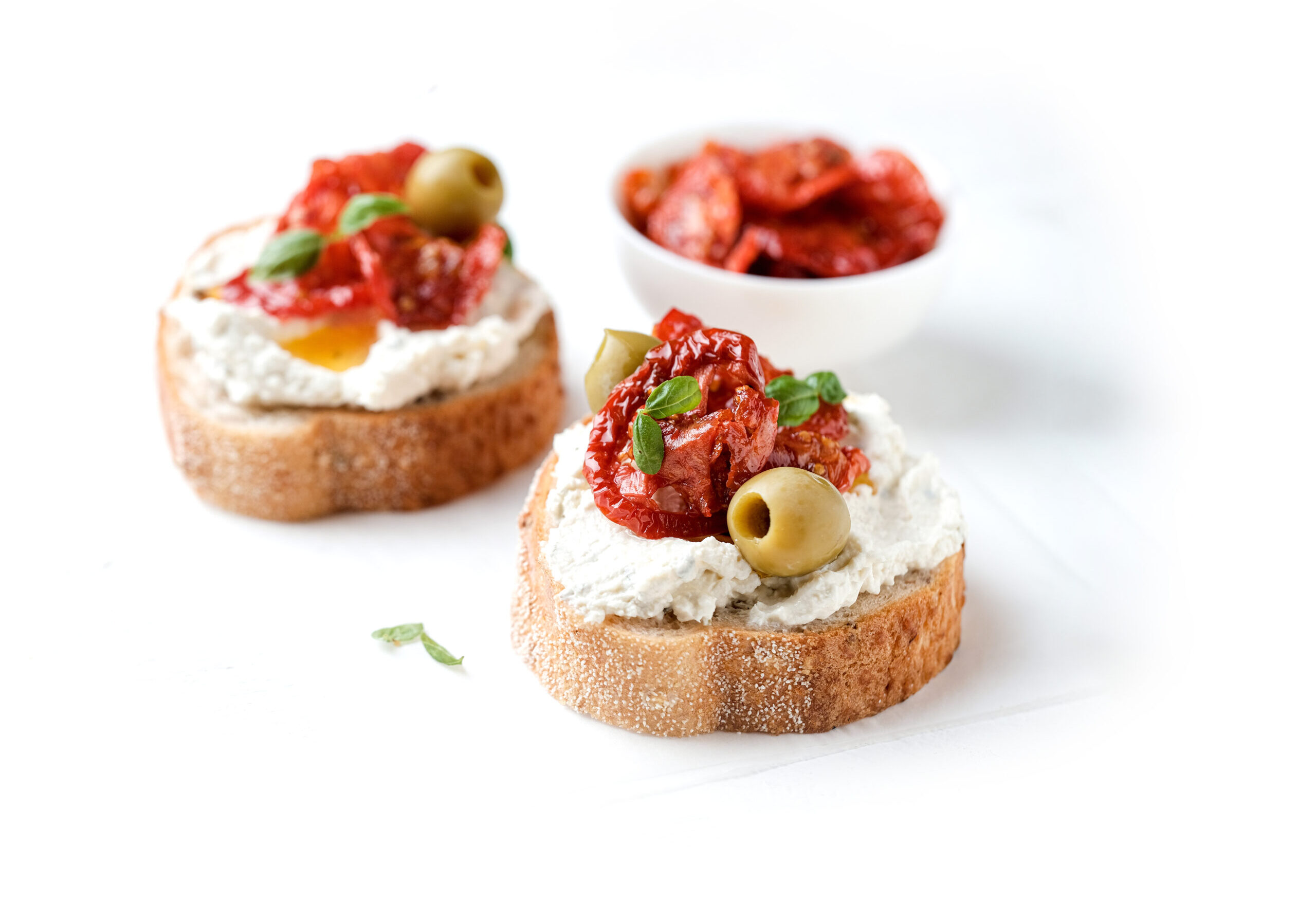 Two bruschettas with ricotta cheese, olive and dried tomatoes on